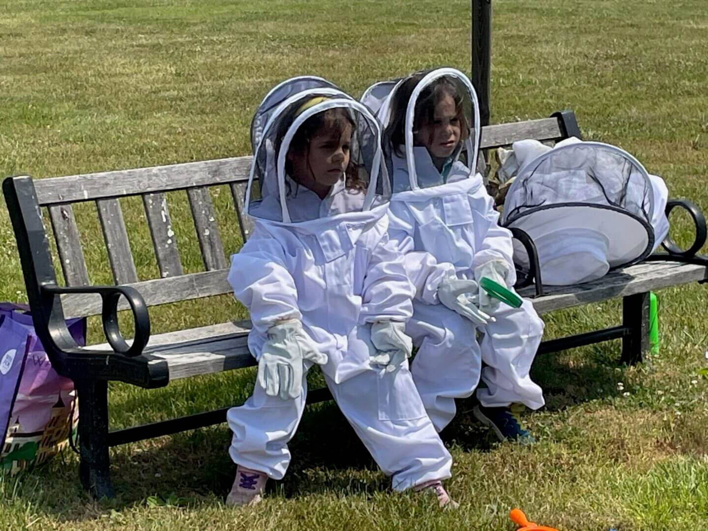 Two children in bee suits sitting on a bench.